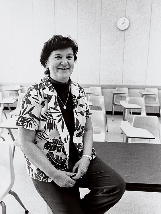 Gertrude Decker Pownall wearing a floral shirt, seated on a classroom desk