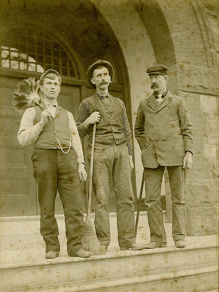 Three men stand with janitorial and digging equipment