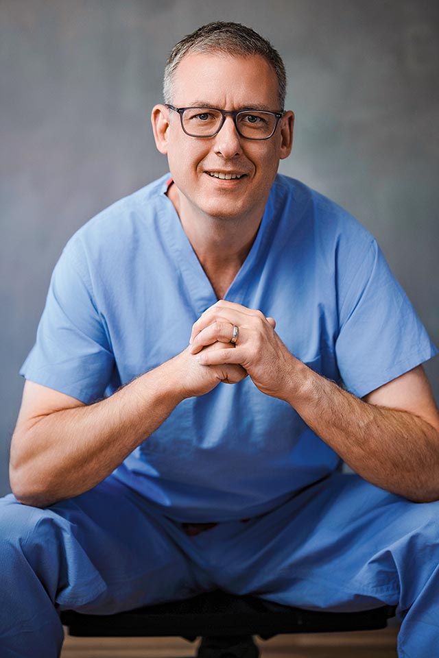 Headshot of Marc David Munk, wearing blue hospital scrubs