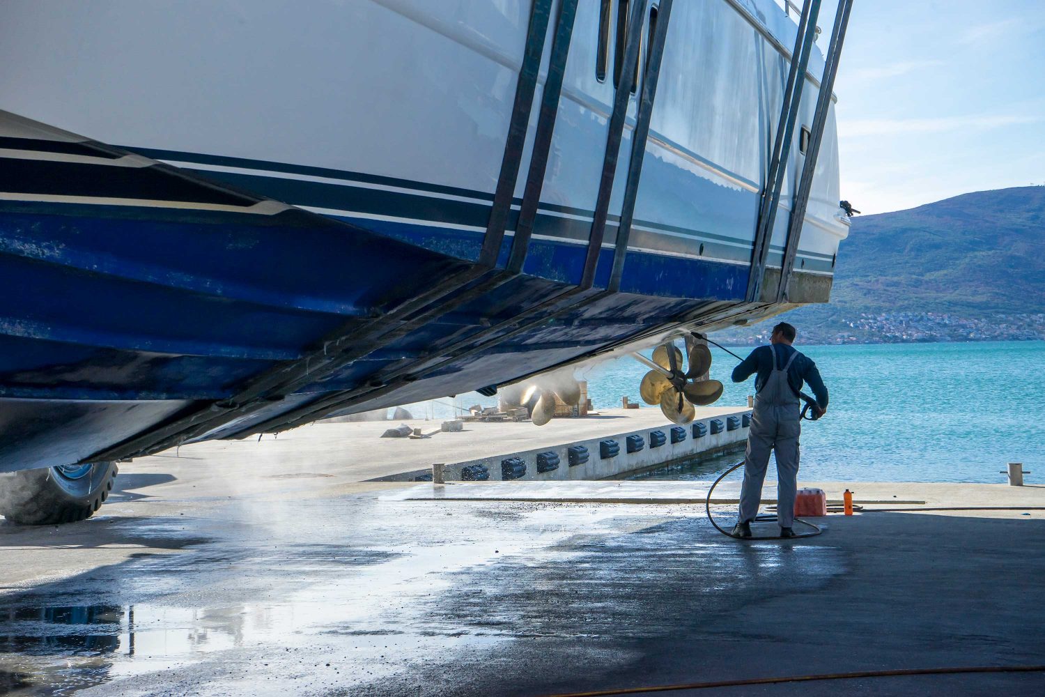 Montenegro, Tivat, October 30 2017. Man is working at the Navar Boatyard. He is using a pressure washer to clean the bottom of the boat while it is in dry dock. He is removing barnacles from the prop and shaft. Boats need routine cleaning and maintenance.