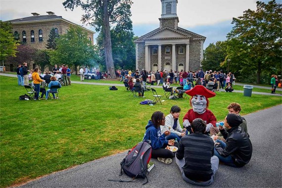 Raider sits with students eating on the Academic Quad