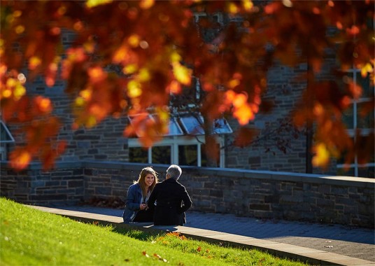 Student speaks with family member framed by autumn leaves