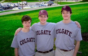 Three young men in Colgate t-shirts and baseball caps on a staircase