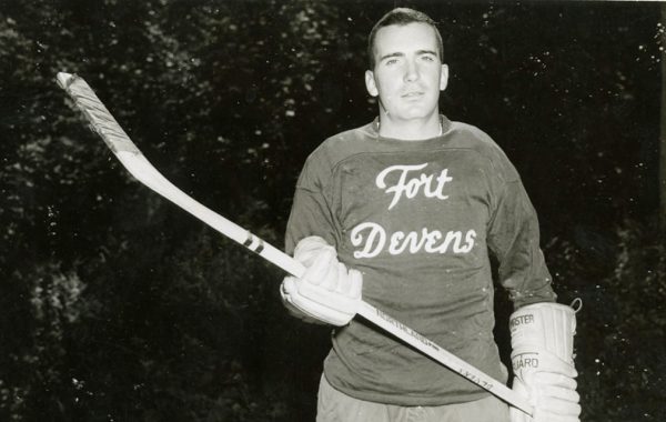 Steve Riggs holding a hockey stick in his Fort Devens uniform