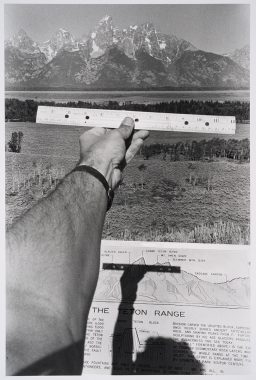 Black and white image of a hand holding a ruler up to the view of a mountain in the distance