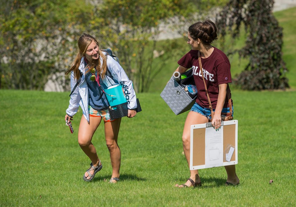 Two students carry items up the hill while chatting
