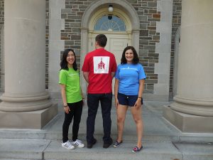 Three students model green, red, and blue t-shirts