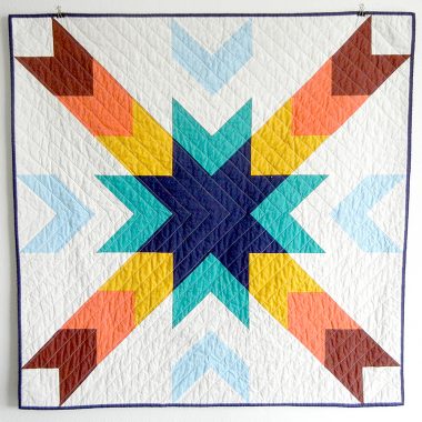 QLT quilt in blues, oranges, and yellow.