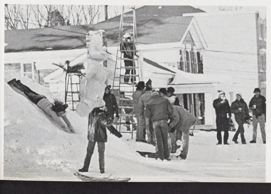 Black and white photo of students building snow sculptures and sliding in the snow