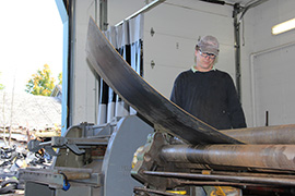 Professor DeWitt Godfrey operating a rolling machine to bend a piece of metal.