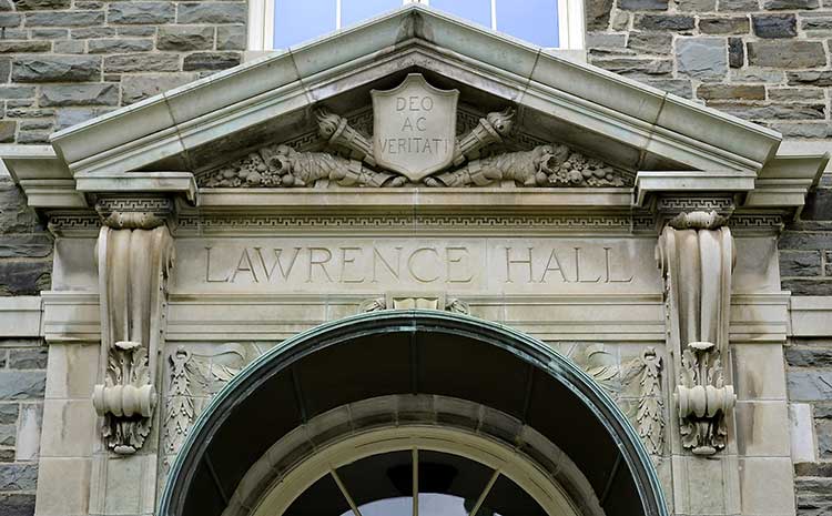 Entrance to Lawrence Hall with a carving of two torches flanking a shield reading Deo ac veritati