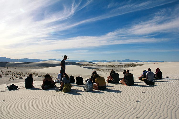 Professor speaking to students sitting in the desert