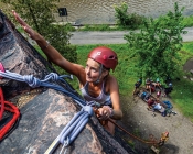 woman reaching up a rock wall in climbing gear