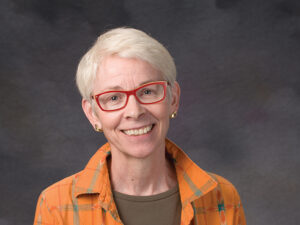 Faye Dudden portrait with short white hair and wearing a yellow shirt