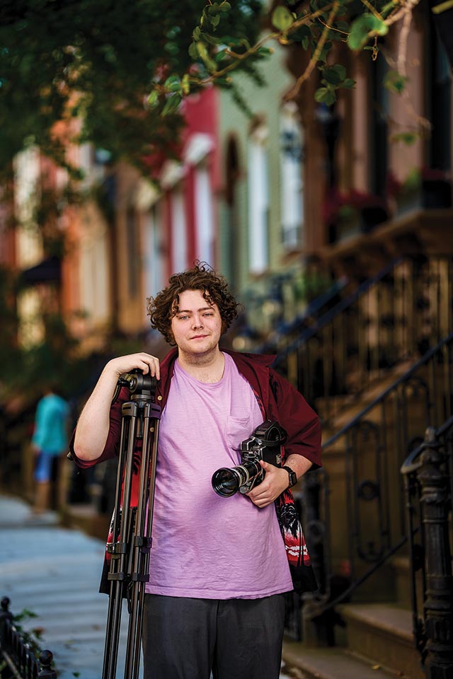 Joe Giordano ’22 poses with camera and tripod on the street.
