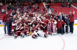 Men's hockey team gather on ice for photo with the trophy