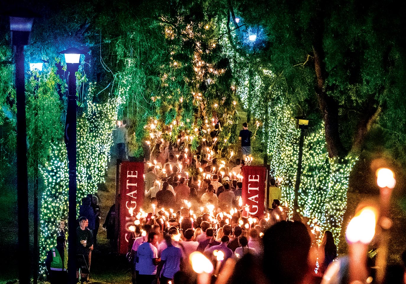 Colgate alumni hold lit torches as they walk through a lit Willow Path during Torchlight Ceremony.