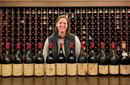 Colgate graduate Julia Gilbert stands with wine collection behind her and with featured bottles on table in front of her