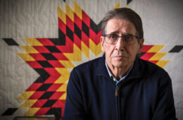 Frank Pommersheim ’65 in a dark sweater and glasses in front of a Native American sunburst quilt
