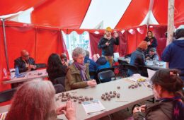 People in a red-and-white-stroped tent make bison beads sitting at tablesBison Bead Project