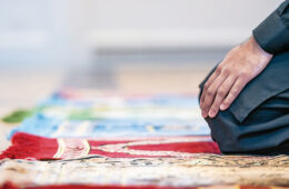 A hand on a knee on a prayer rug