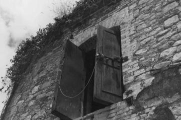 Black & White photograph titled "Windows Slave Jail," a stone building with open wooden doors and plants growing on the roof.