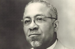 Black-and-white portrait of African-American man wearing wire-rimmed glasses, close-cropped hair, and a goatee