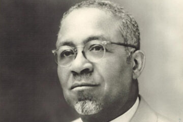 Black-and-white portrait of African-American man wearing wire-rimmed glasses, close-cropped hair, and a goatee