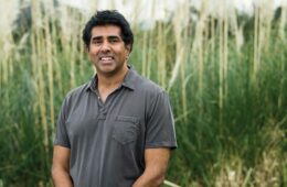 Portrait of Jay Chandrasekhar standing in front of a blurred-out field of tall grasses
