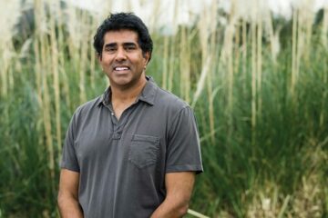 Portrait of Jay Chandrasekhar standing in front of a blurred-out field of tall grasses