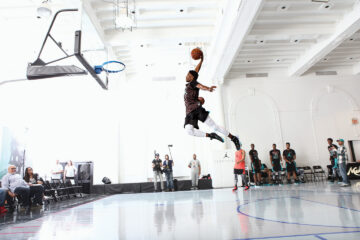 Male basketball player soars through the air making a dunk shot. Photo by Jon Lopez.