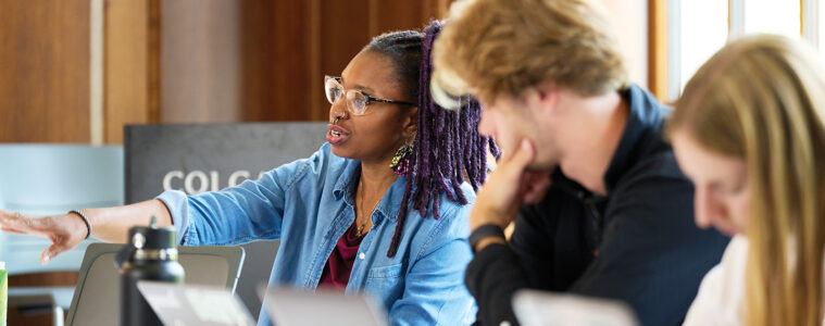 Professor Dominique Hill gestures at a seminar table, while two students listen to her right.