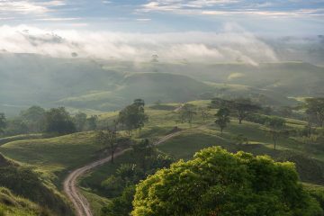 Dirt road in a Colombian landscape at sunrise with fog between the mountains in the background.