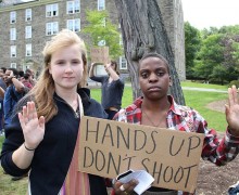 Students raise their hands while displaying a sign that reads hands up, don't shoot