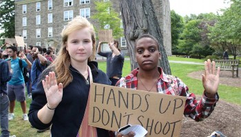Students raise their hands while displaying a sign that reads hands up, don't shoot