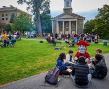 Raider sits with students eating on the Academic Quad