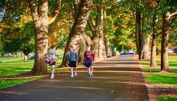 Three students in athletic attire walk along Oak Drive.