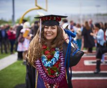 Sahara-Yvette Zamudio '17 in her commencement cap, gown, and colorful flowered leis on Crown field.