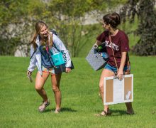 Two students carry items up the hill while chatting