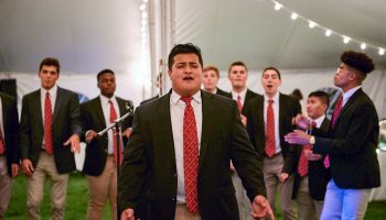 Student sings a solo with his a capella group under the lights in a tent