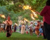 Native American men and women hold torches on a lawn during daylight hours