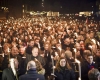 A crowd of men and women bearing small torches at night