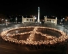 A crowd of people holding torches stands in the form of a peace symbol at night