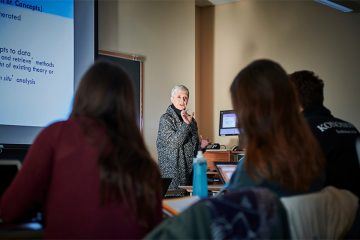 Colgate Professor Ellen Kraly lectures at the front of a classroom