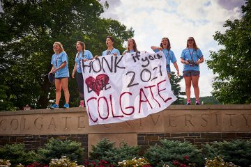 Students stand on wall beside Oak Drive welcoming members of the Class of 2021 to campus