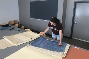 Student stands at table and leans over blueprints