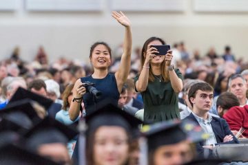 Family members with cameras wave to graduating seniors at commencement